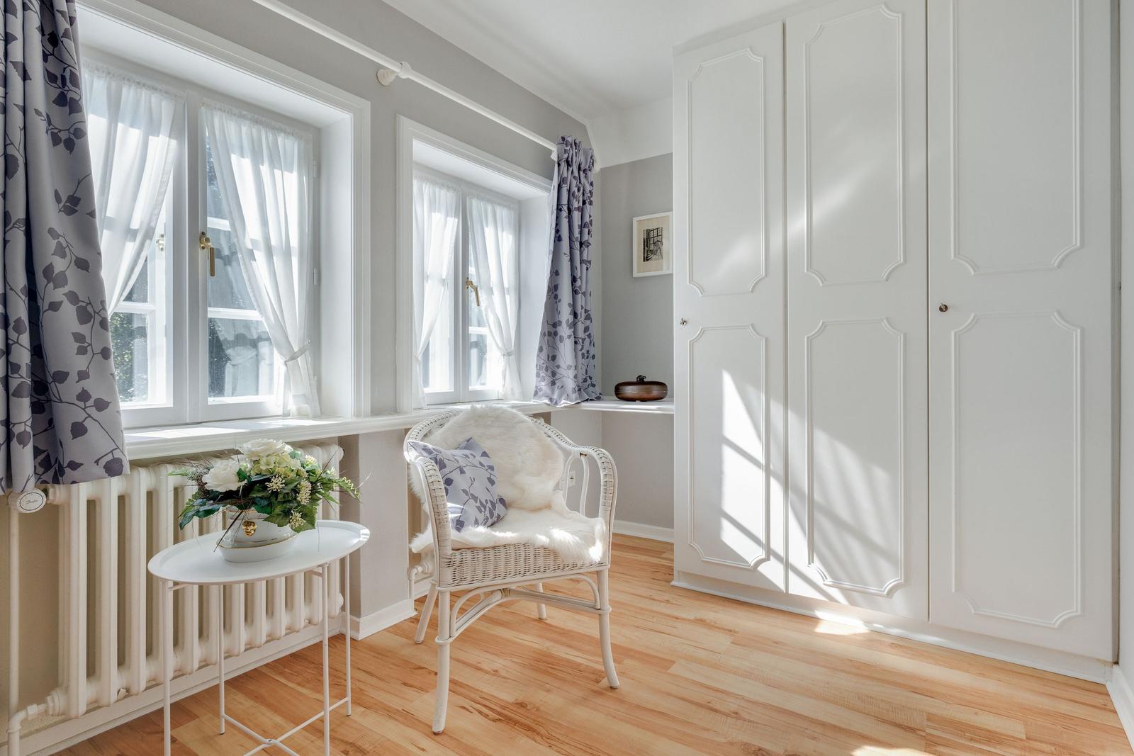 Room with two windows, white closet, and chair with fur cushion.