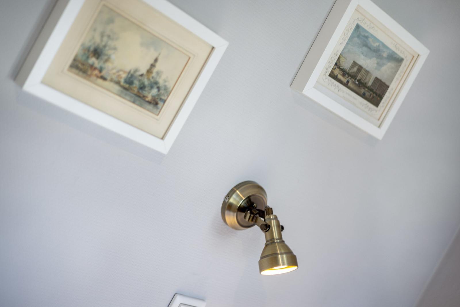 Two framed pictures on the wall and a wall lamp with a brass shade.