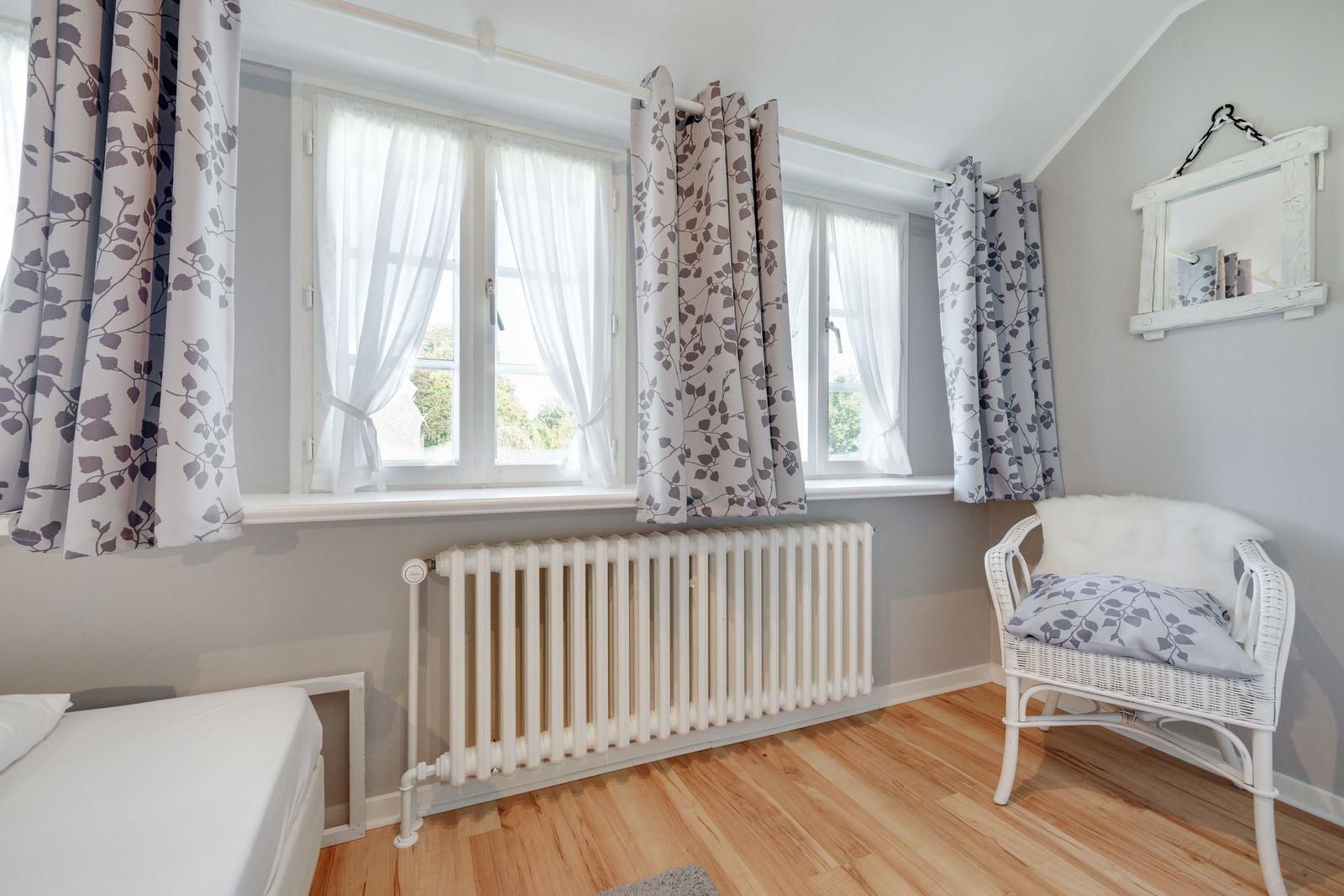 Room with bed, windows, radiator, and chair with cushion.