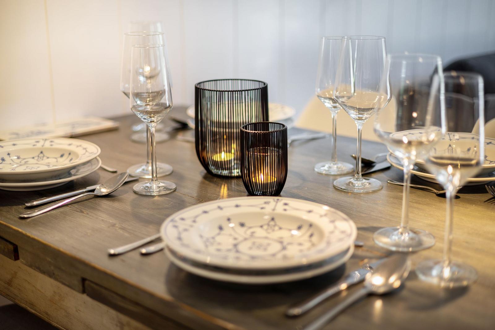 Gedeckter Holztisch mit Teller, Gläsern und Kerzenhaltern.