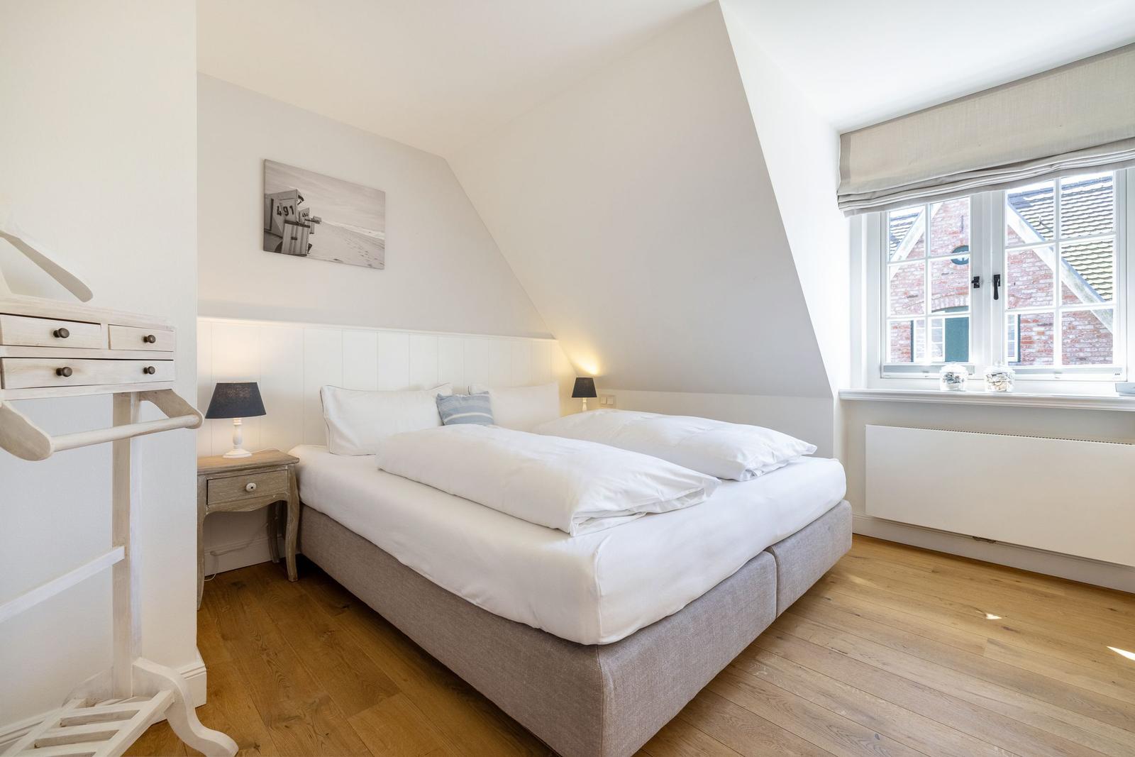 Schlafzimmer mit Doppelbett, Holzboden und Fenster mit Blick auf Gebäude.