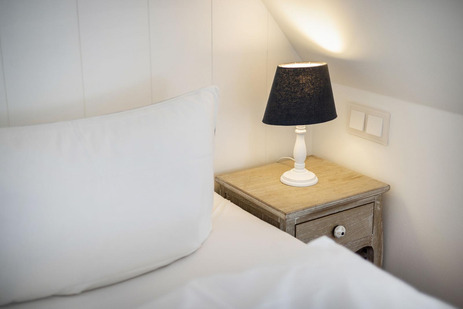 Schlafzimmer mit Bett, Nachttisch und Lampe unter Dachschräge.