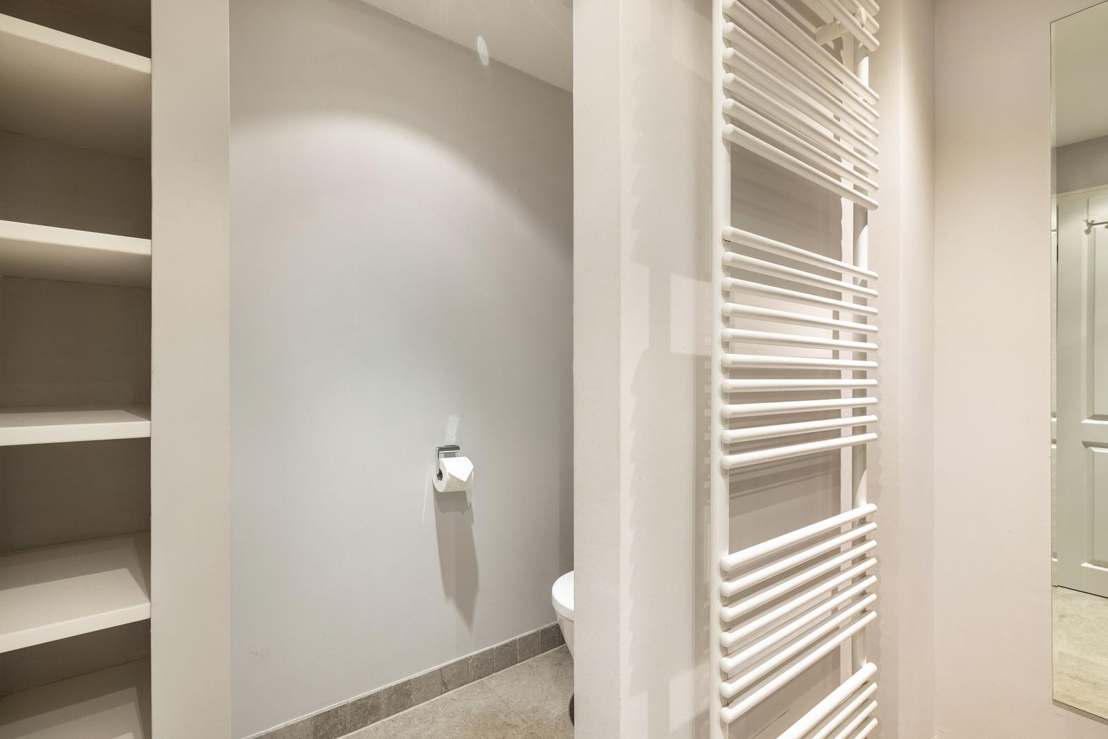 Badezimmer mit Toilette, Heizkörper und offenen Regalen.