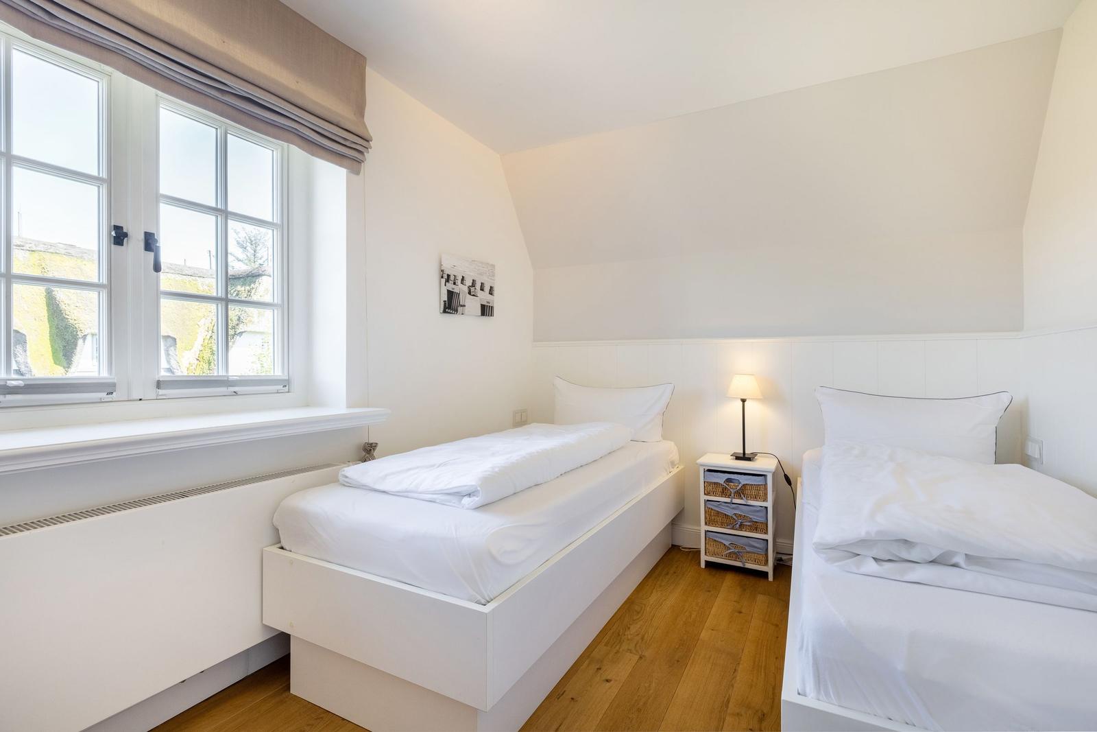 Zwei Einzelbetten, Fenster, Nachttisch mit Lampe und Holzboden.