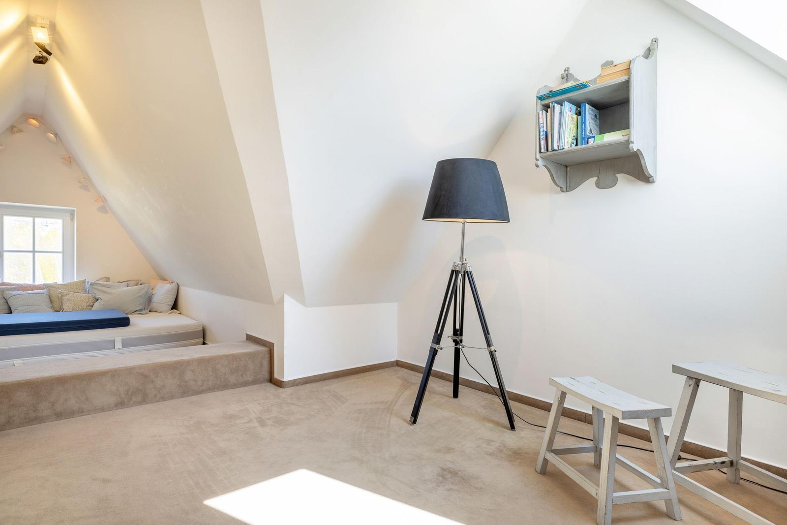 Dachgeschosszimmer mit Schlafcouch, Stehlampe und Wandregal.