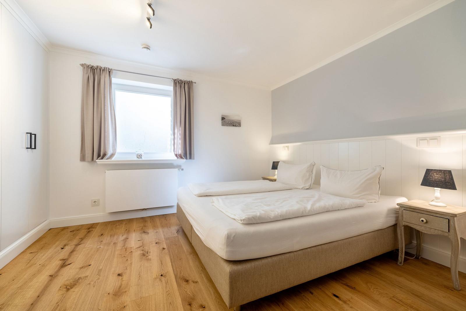 Schlafzimmer mit Doppelbett, Holzboden und Fenster mit Vorhängen.
