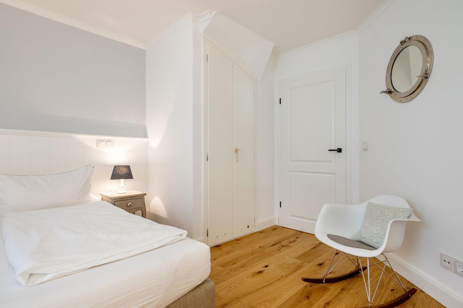 Schlafzimmer mit Bett, Nachttisch, Stuhl und runden Spiegel an der Wand.
