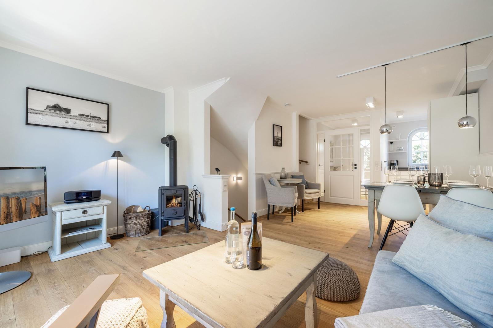 Wohnbereich mit Kamin, Sofa und Esstisch. Holzboden und helle Wände.