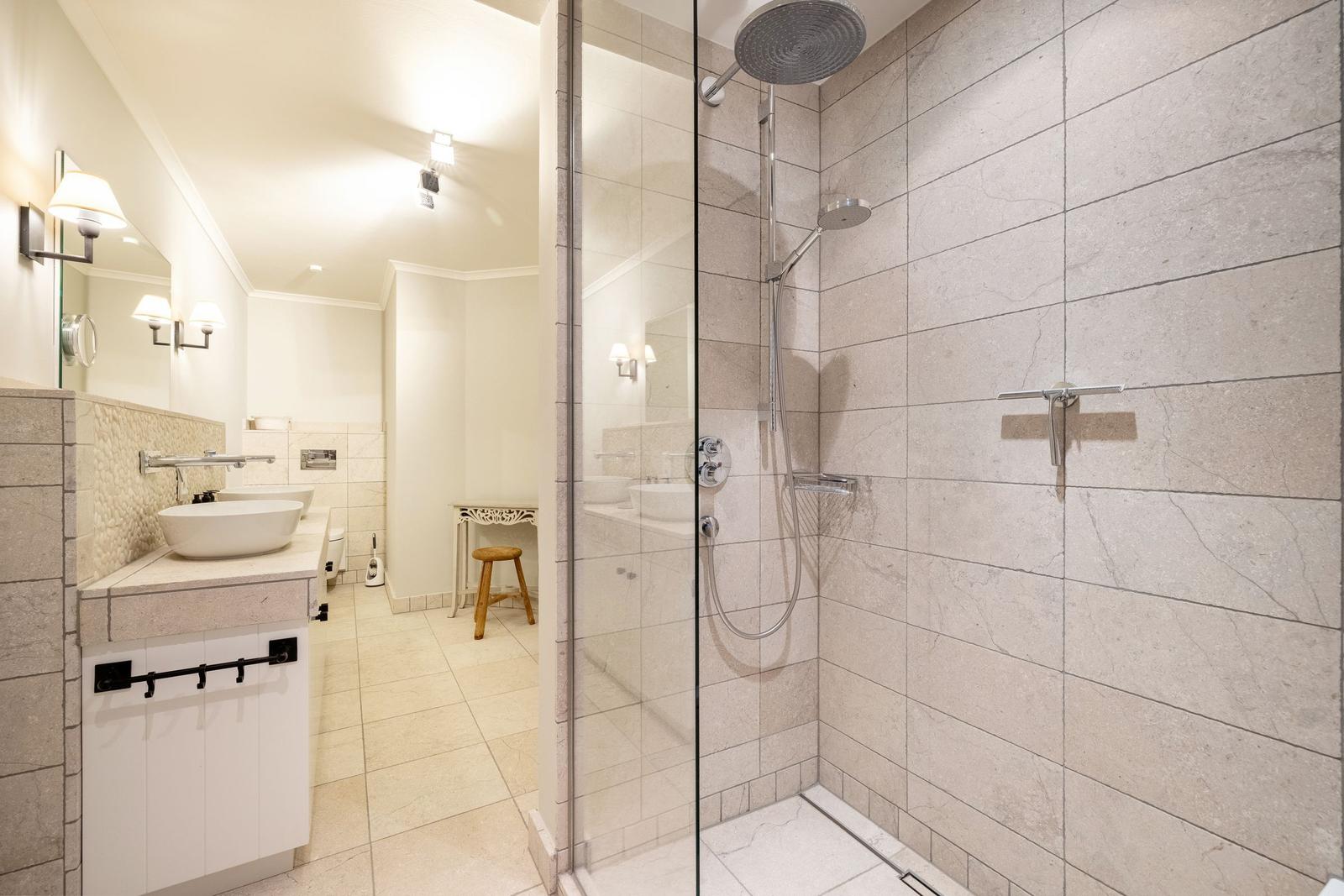 Dusche mit Glaswand, Waschbecken und Spiegel im Badezimmer