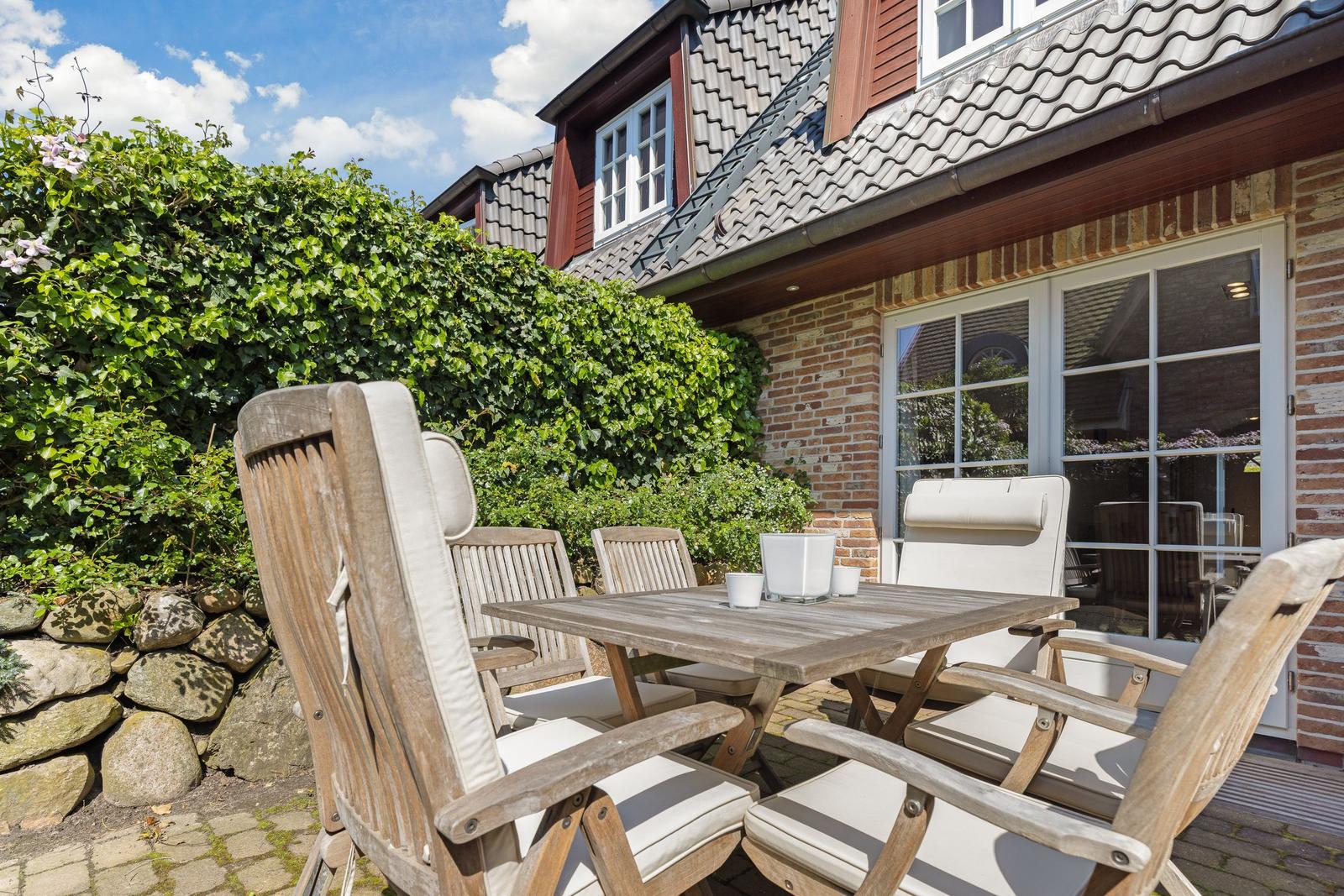 Terrasse mit Holztisch und Stühlen vor einem Haus mit Ziegelfassade und Glasfront.