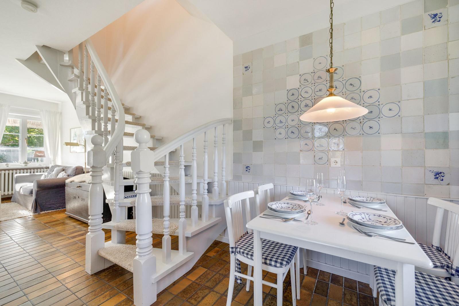 Dining room with table, chairs, and tiled wall. Stairs lead to living area.