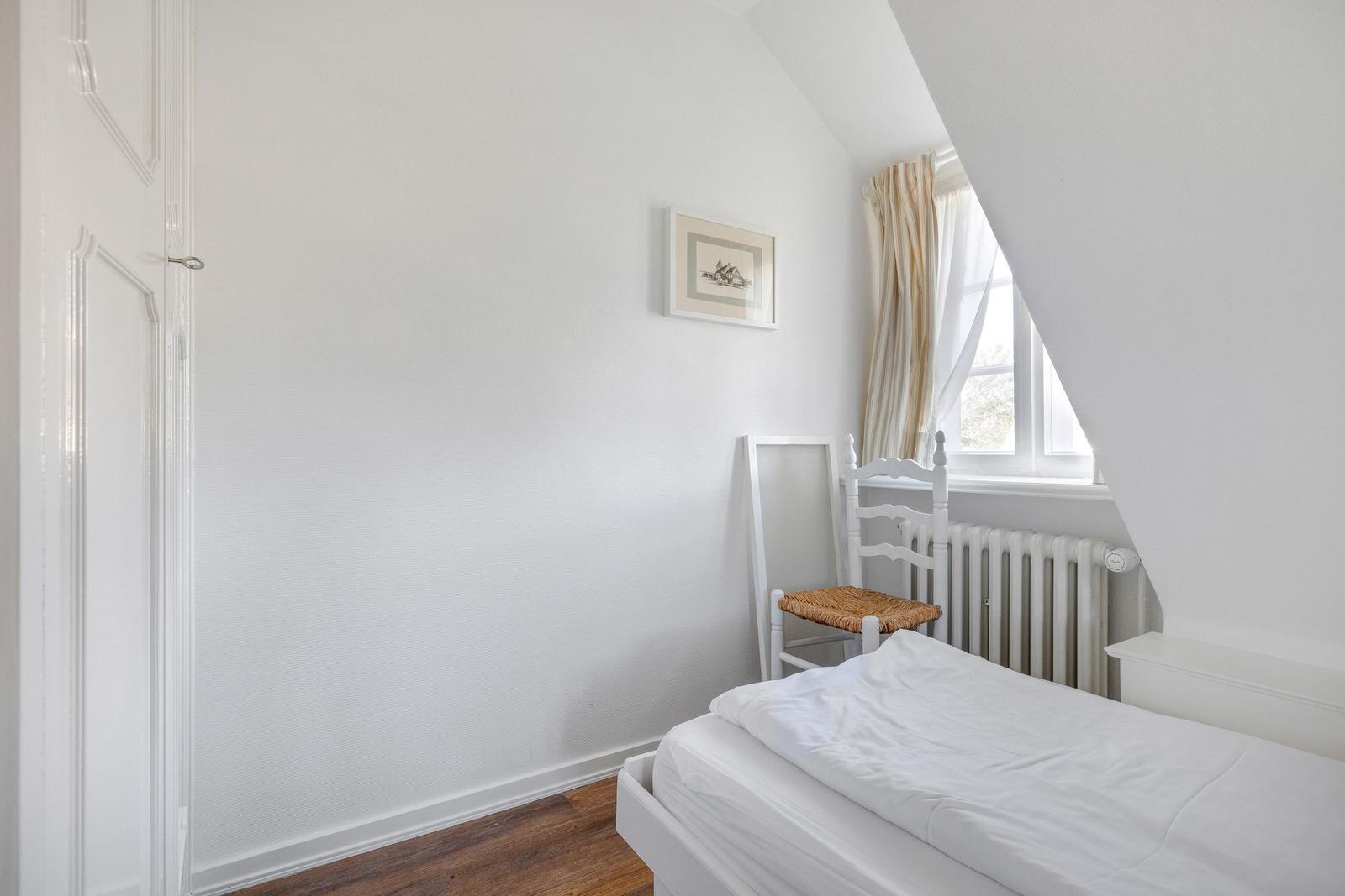 Bedroom with white bed, chair, and window with curtains.