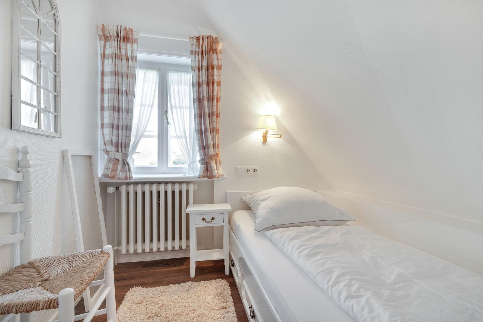 A bedroom with a bed, a nightstand, and a window with curtains.