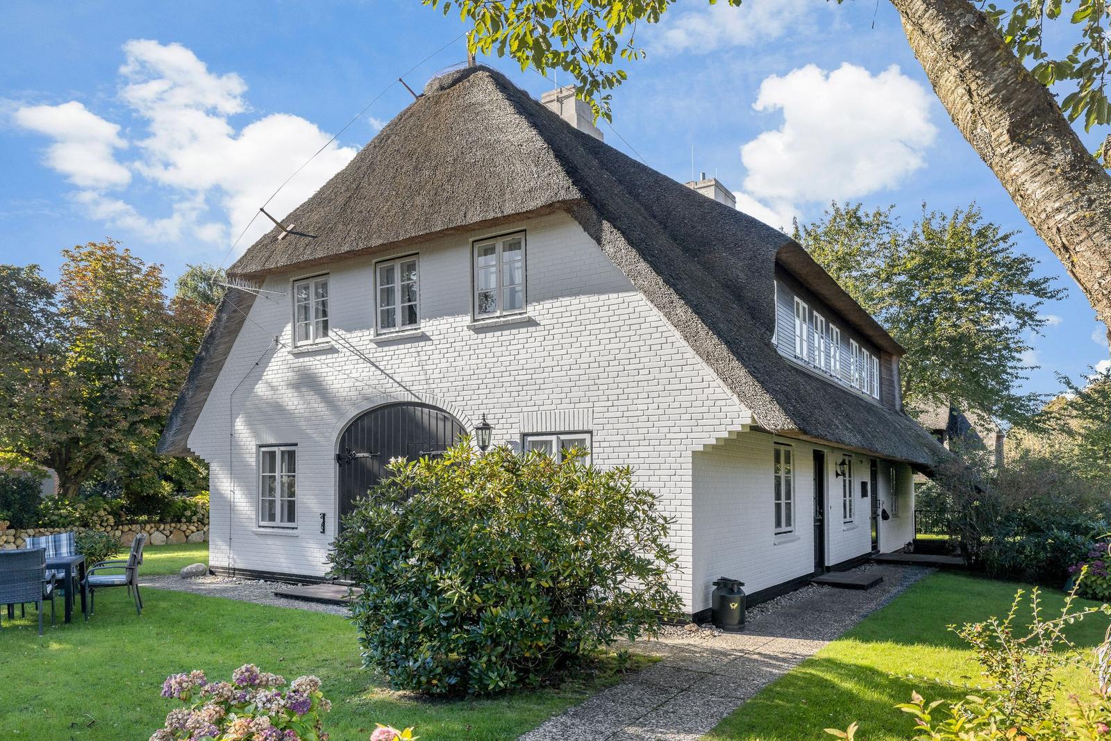 White house with thatched roof and garden. Terrace and plants are visible.