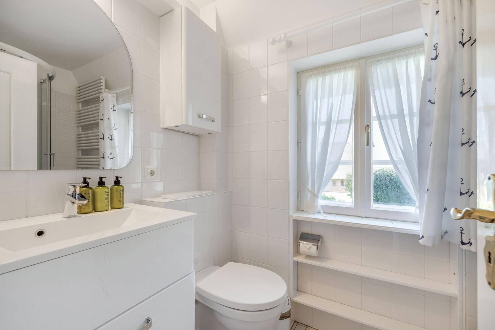 Bathroom with sink, toilet, and window with curtains.