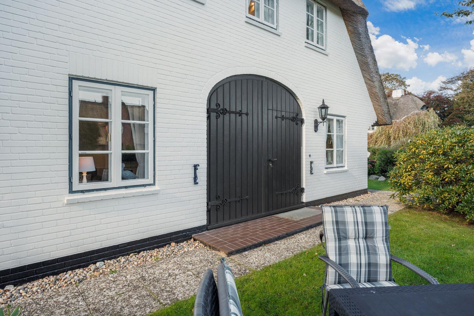 House with white facade, black door, and garden furniture.