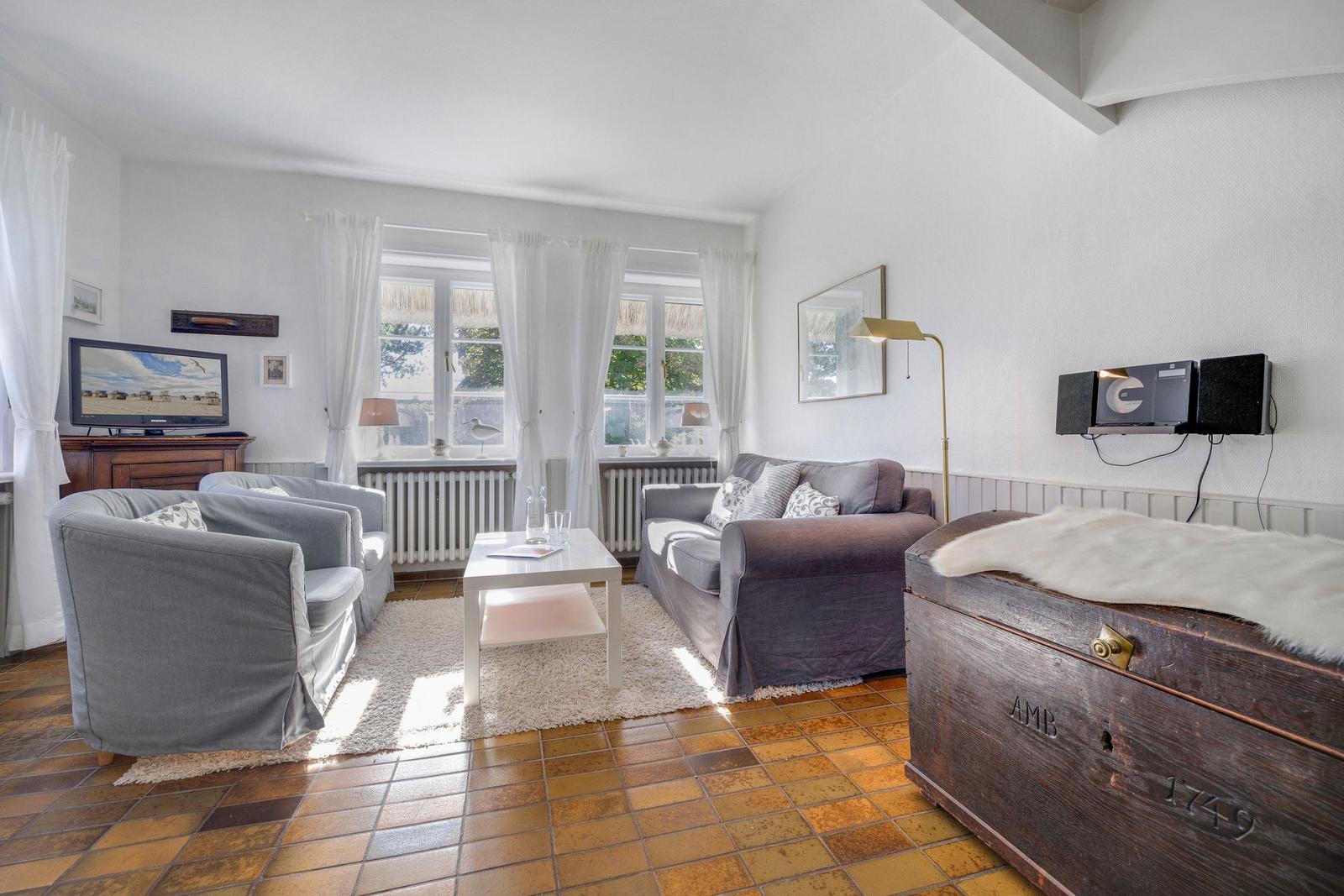 Living room with sofa, armchairs, TV, and old trunk.