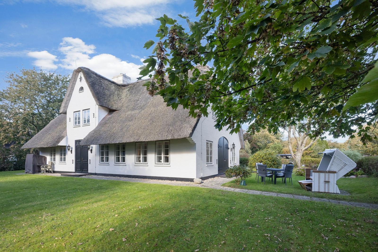 White cottage with thatched roof and garden area with table and chairs.