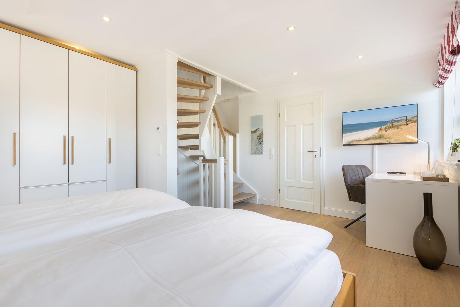 Schlafzimmer mit Bett, Schrank und Arbeitsplatz mit Fernseher.
