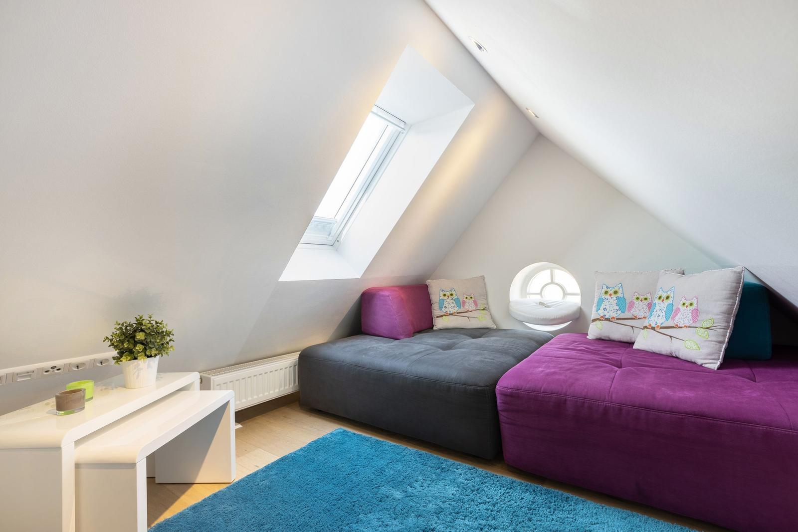 Dachgeschosszimmer mit Schlafcouch, Dachfenster und runder Fensteröffnung.