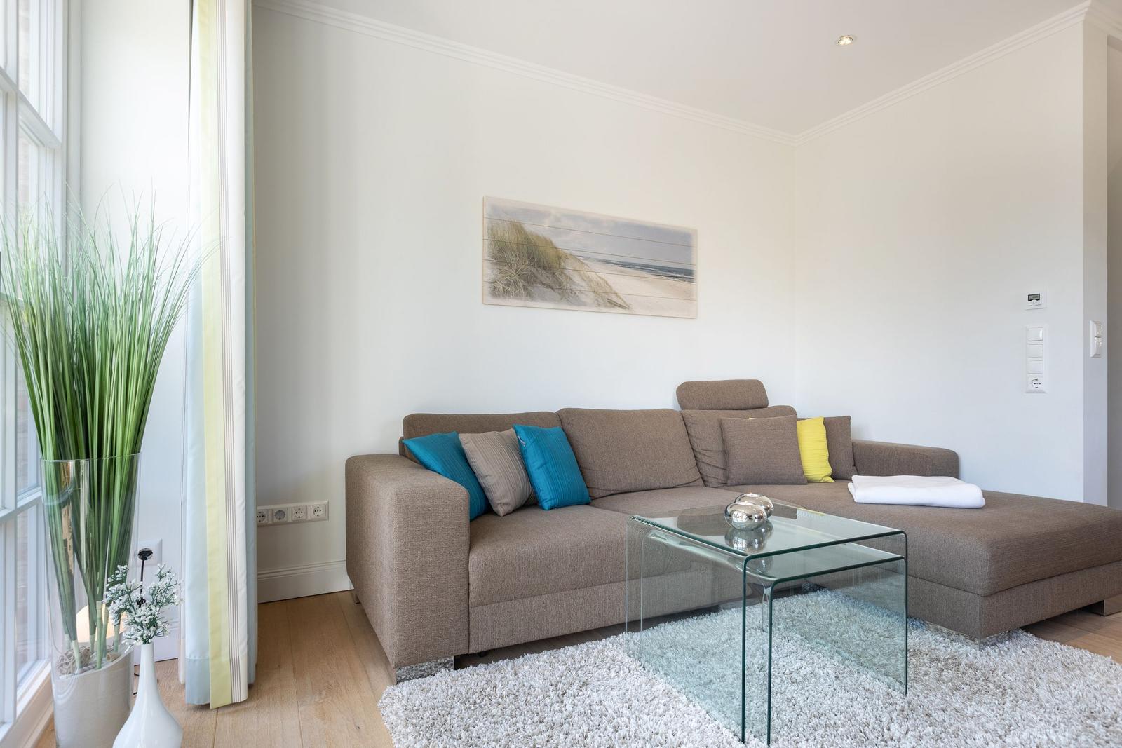 Ein Wohnzimmer mit braunem Sofa, Glas-Tisch und Wandbild.