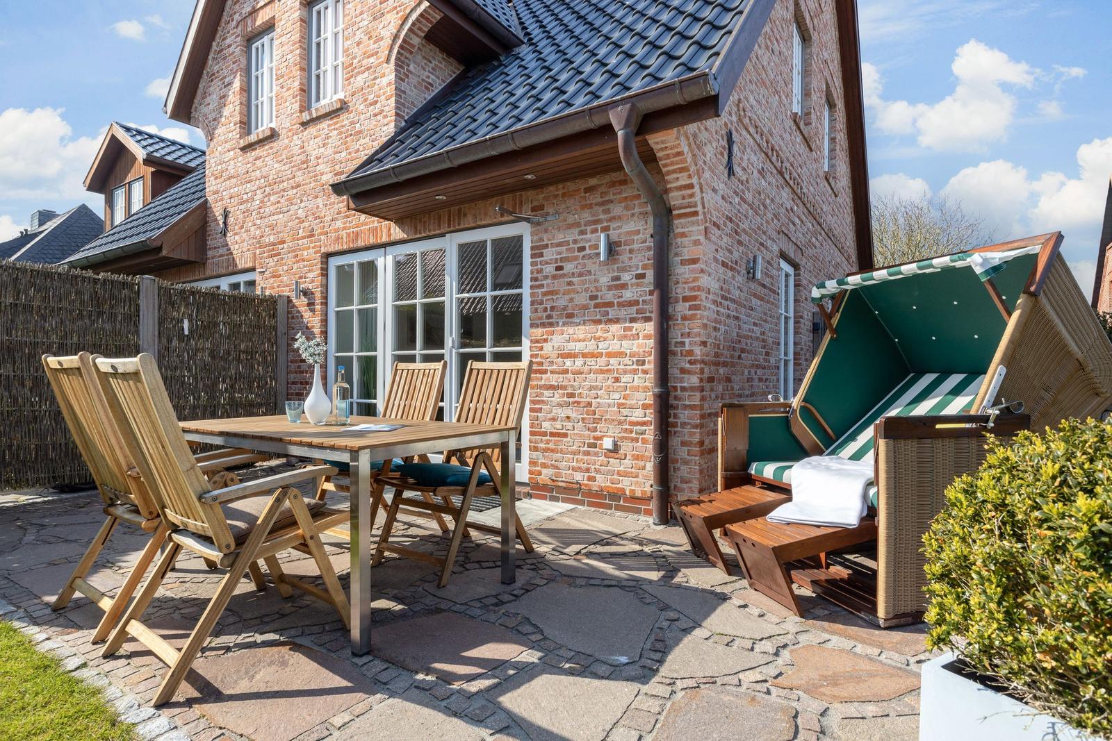 Terrasse mit Holztisch, Stühlen und Liege unter Sonnenschutz.