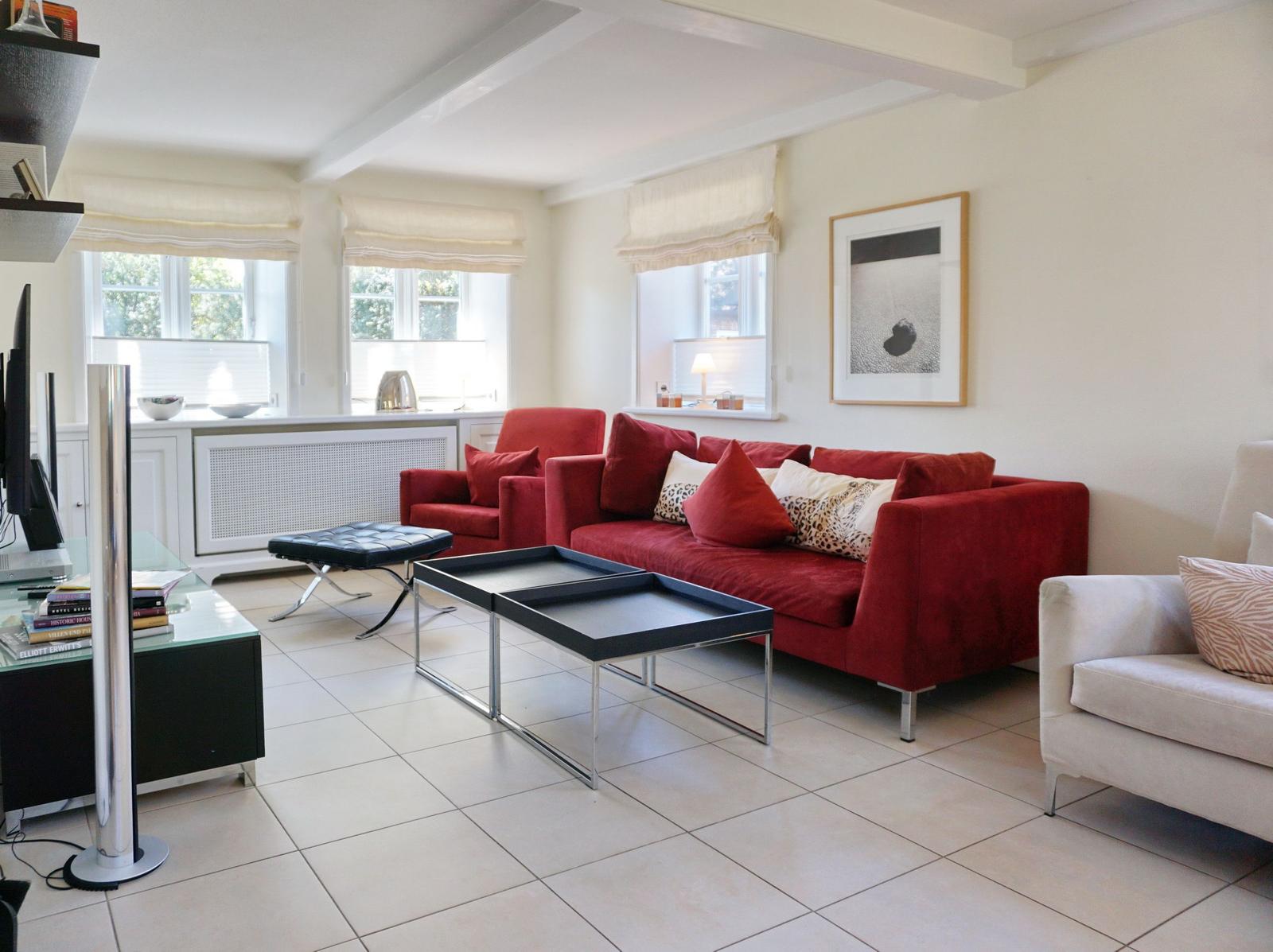 Wohnzimmer mit rotem Sofa, weißen Wänden und Fenstern mit Rollläden.