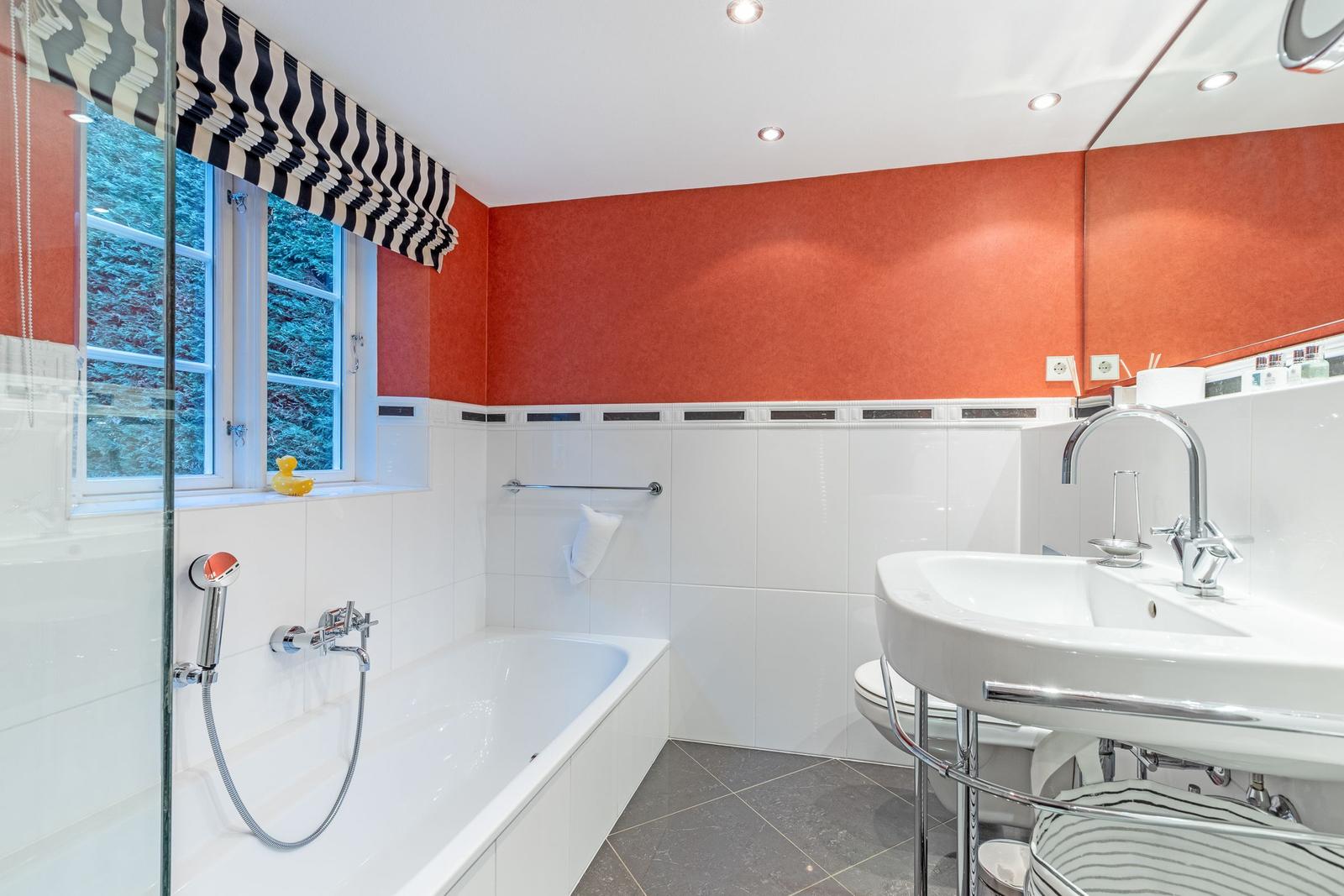 Bad mit Badewanne, Waschbecken und Fenster mit Blick auf Wald.
