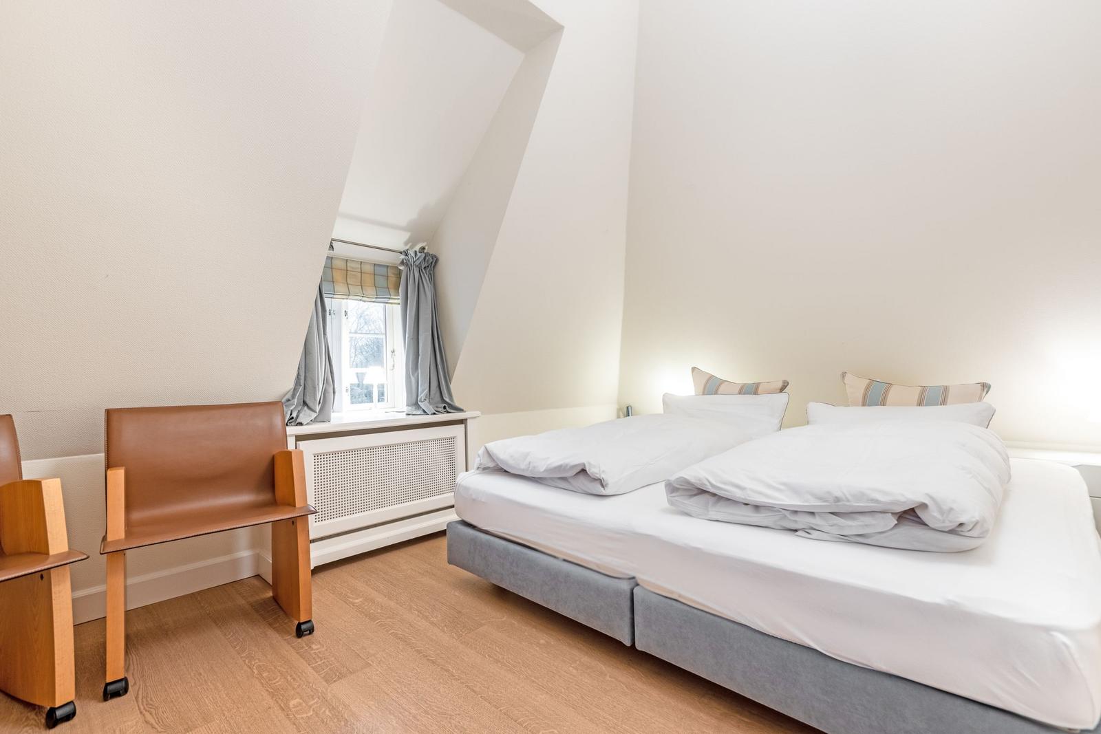 Schlafzimmer mit Doppelbett, Holzboden und Fenster mit Vorhängen.