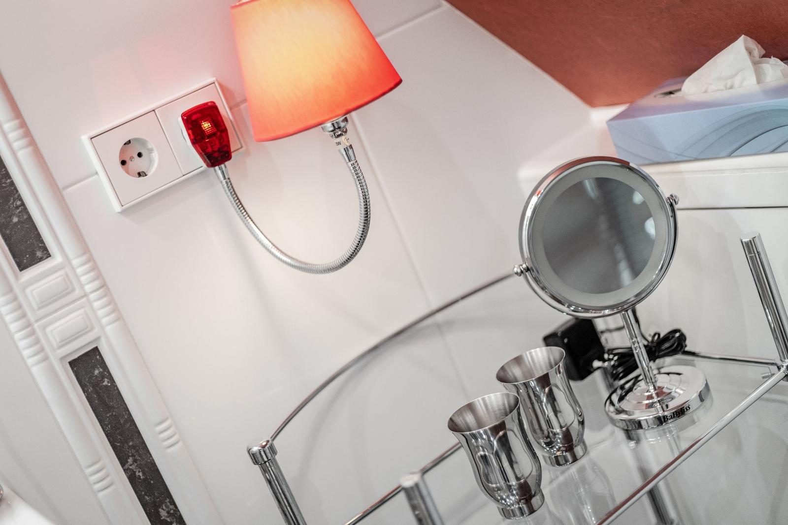 Badezimmer mit Spiegel, Metallbecher und Wandlampe.