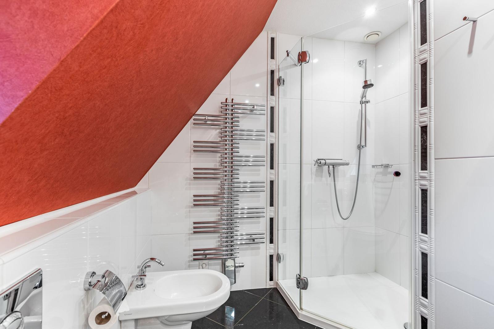Badezimmer mit Dusche, Waschbecken und Heizkörper an geneigter Wand.