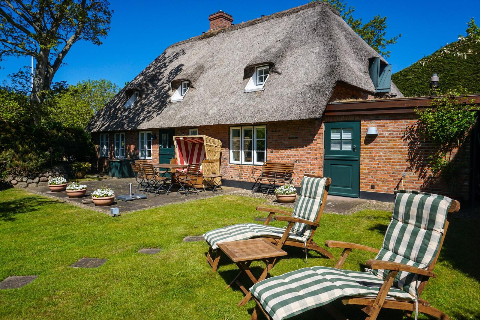 Haus mit Strohdach, Gartenbereich mit Liegestühlen und Terrasse.