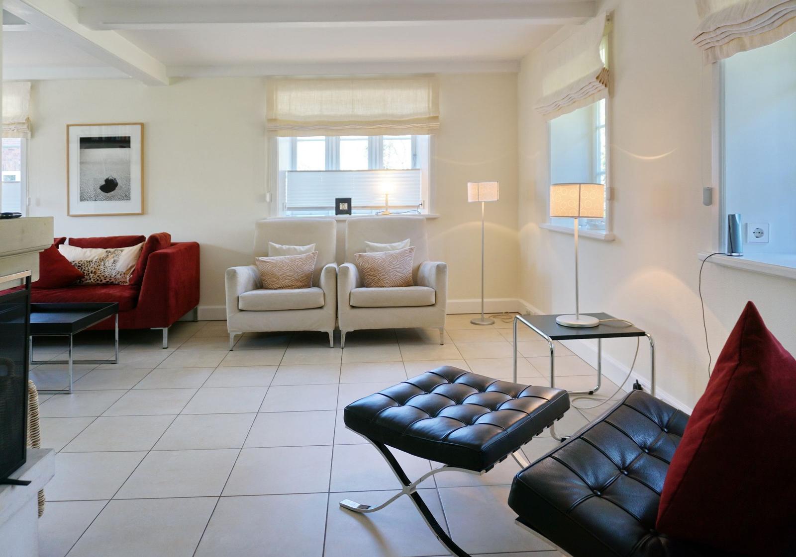 Wohnzimmer mit rotem Sofa, zwei weißen Sesseln und schwarzer Ledercouch.