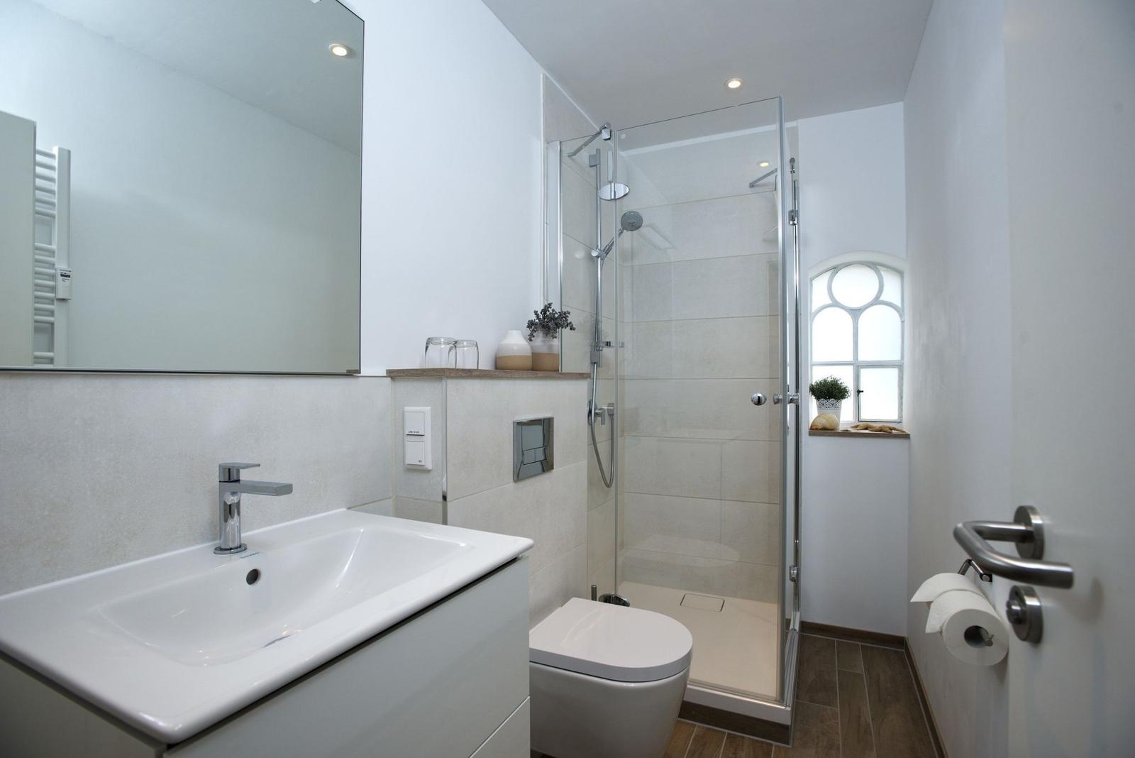 Bathroom with shower, sink, and toilet. Window with plant.