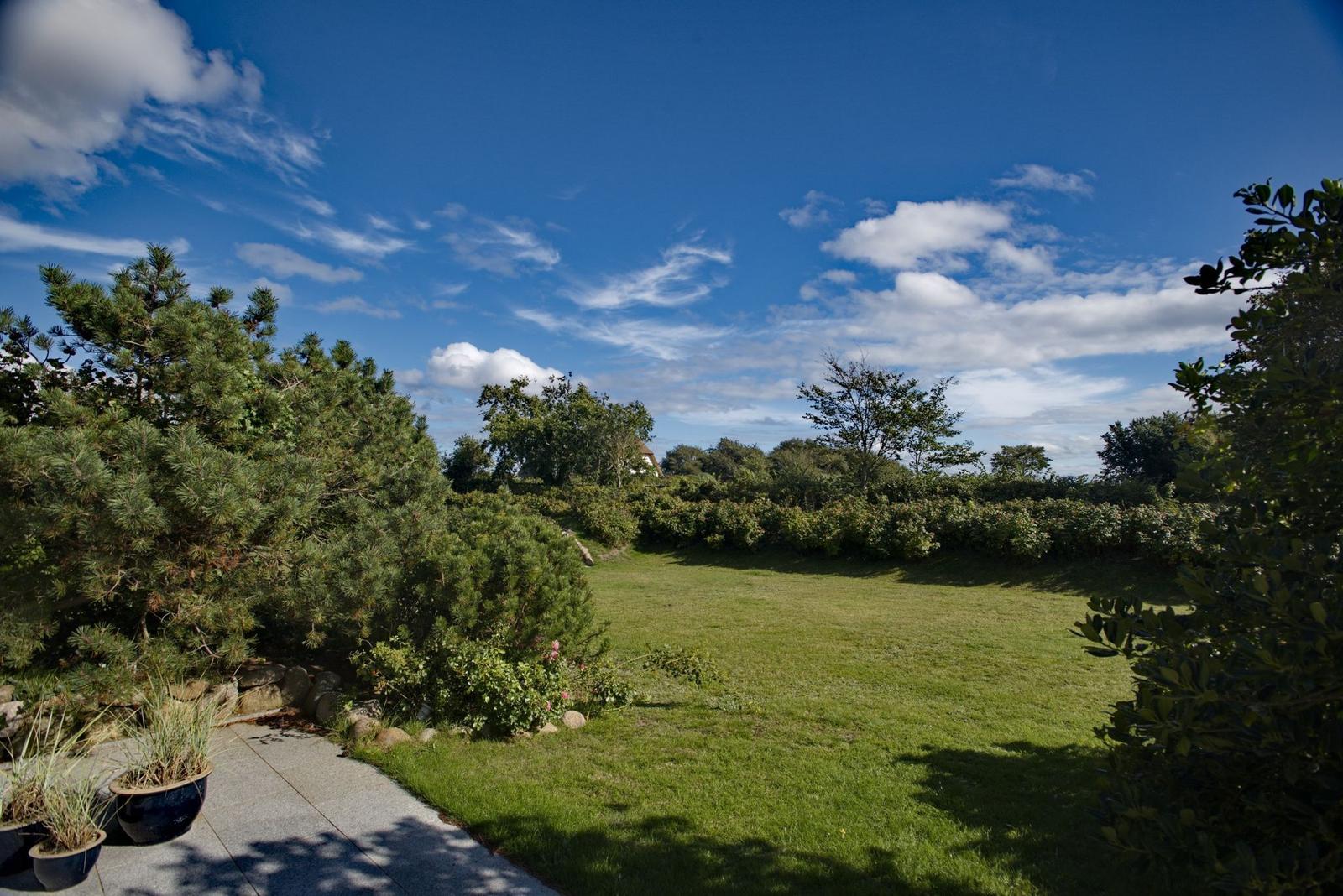 Green lawn area with trees and a path. Sky with white clouds.