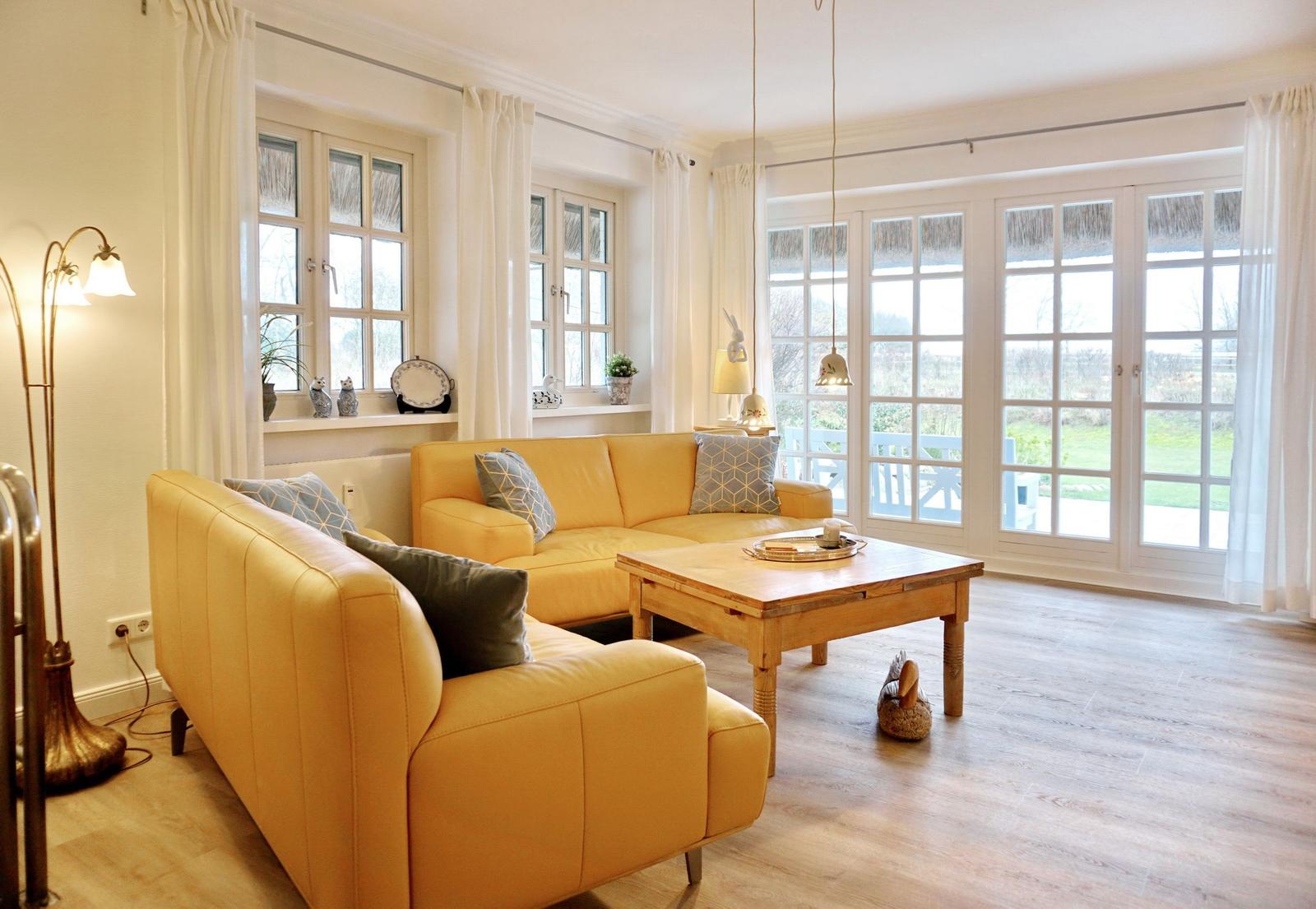 A living room with yellow sofas, wooden table, and windows overlooking the garden.