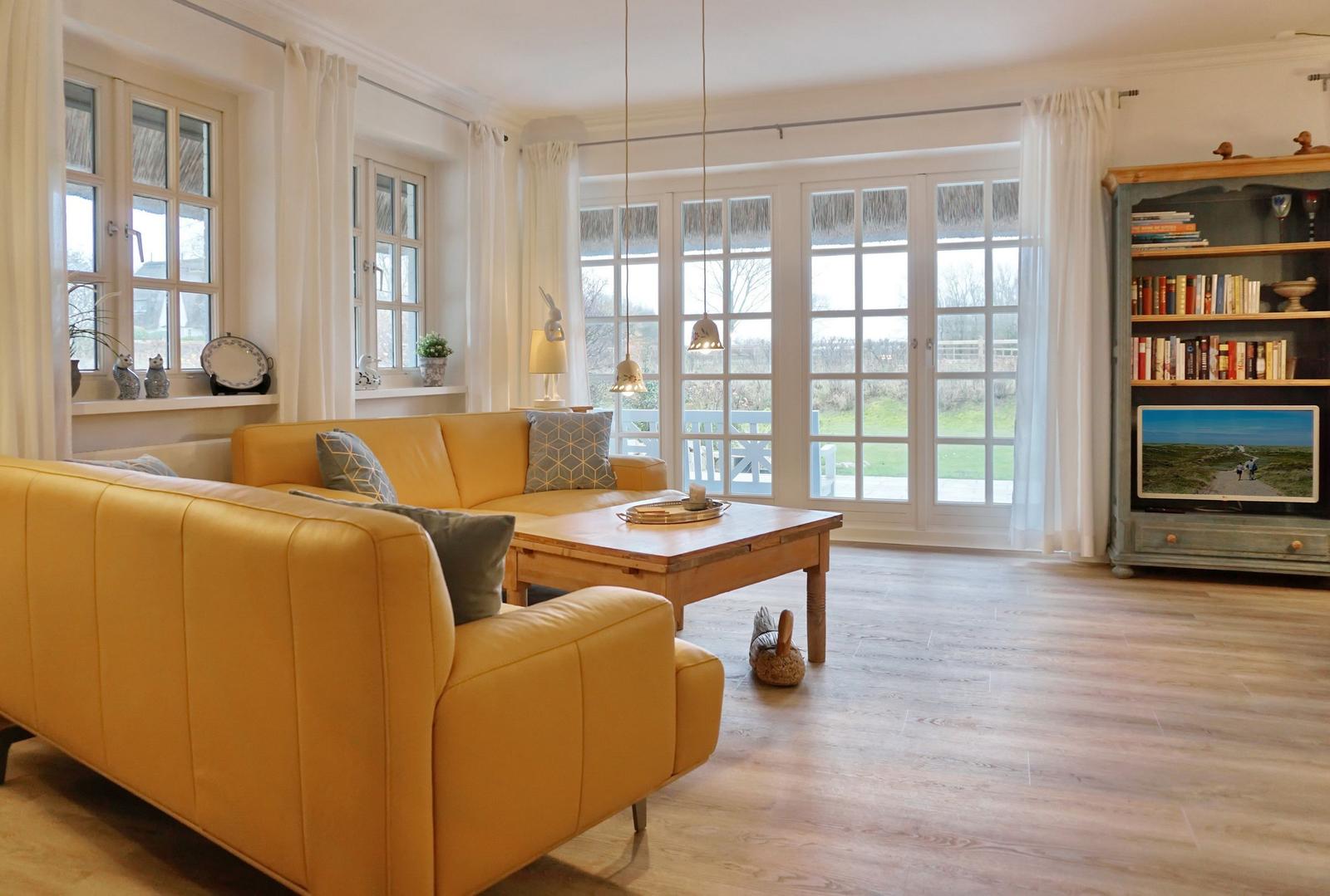 A living room with a yellow sofa, wooden table, and large windows.