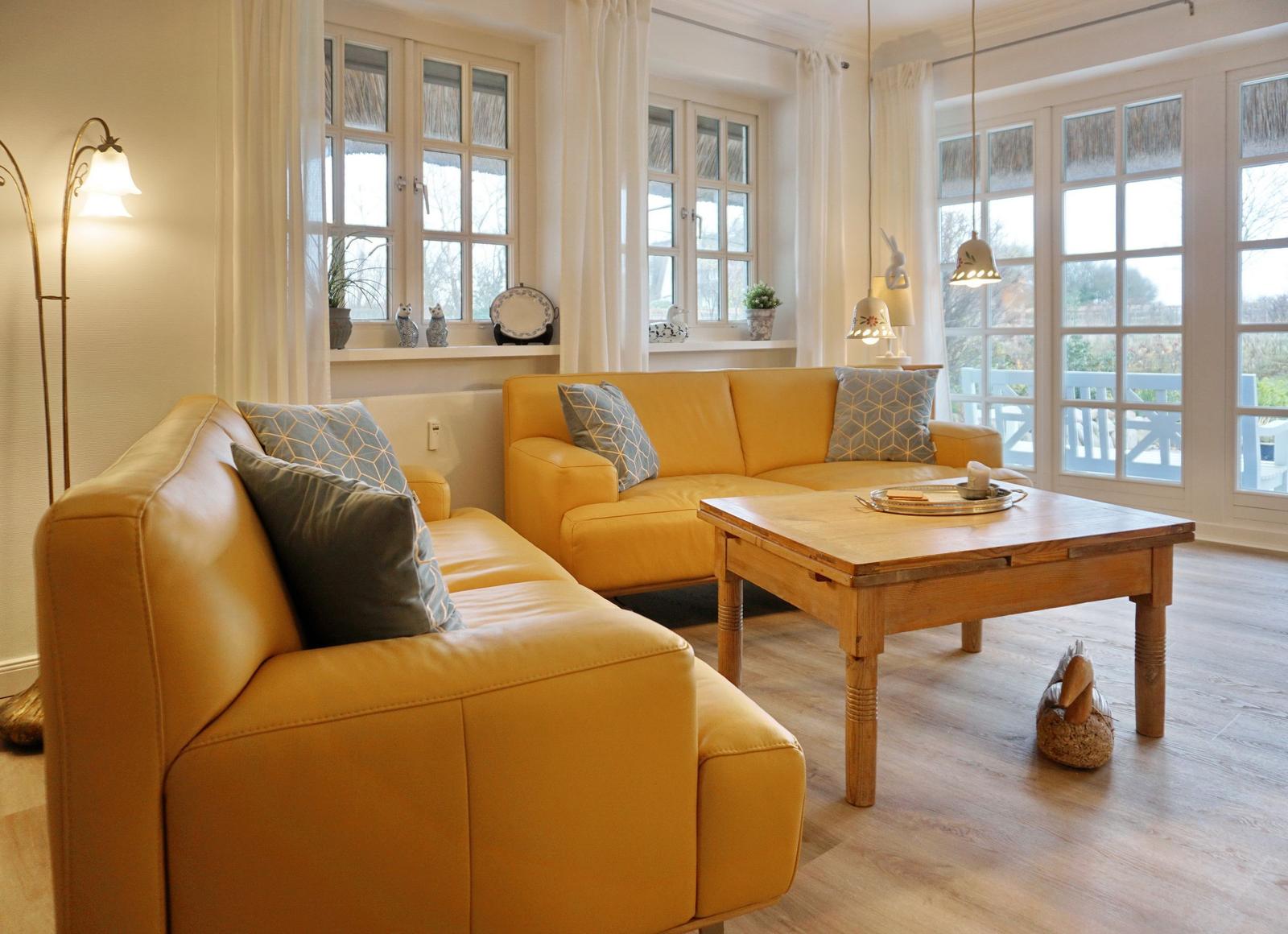 Two yellow sofas with cushions surround a wooden table. Windows and doors offer a view of the garden.