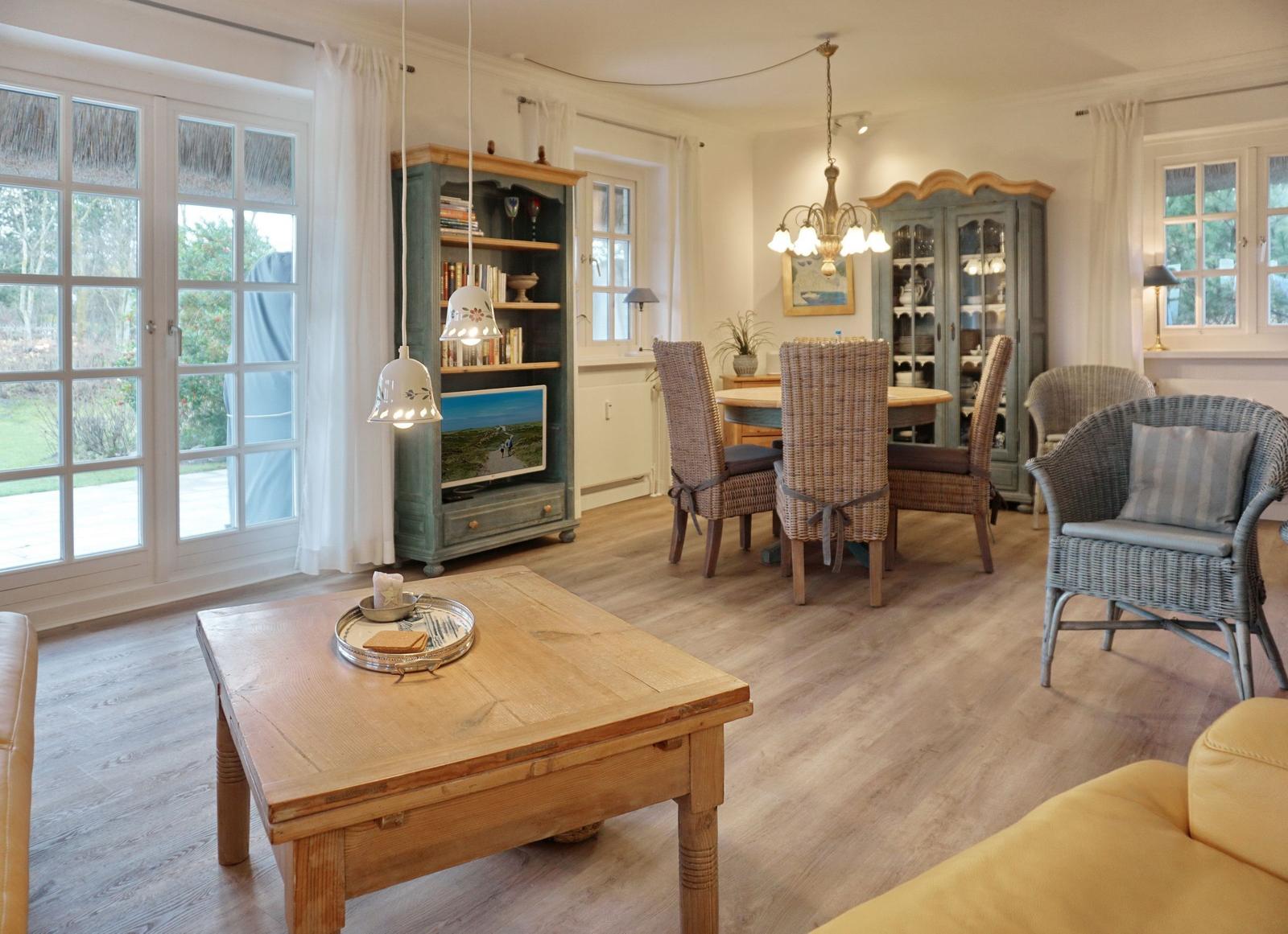 Living and dining area with wooden floor, wicker chairs, and large windows.