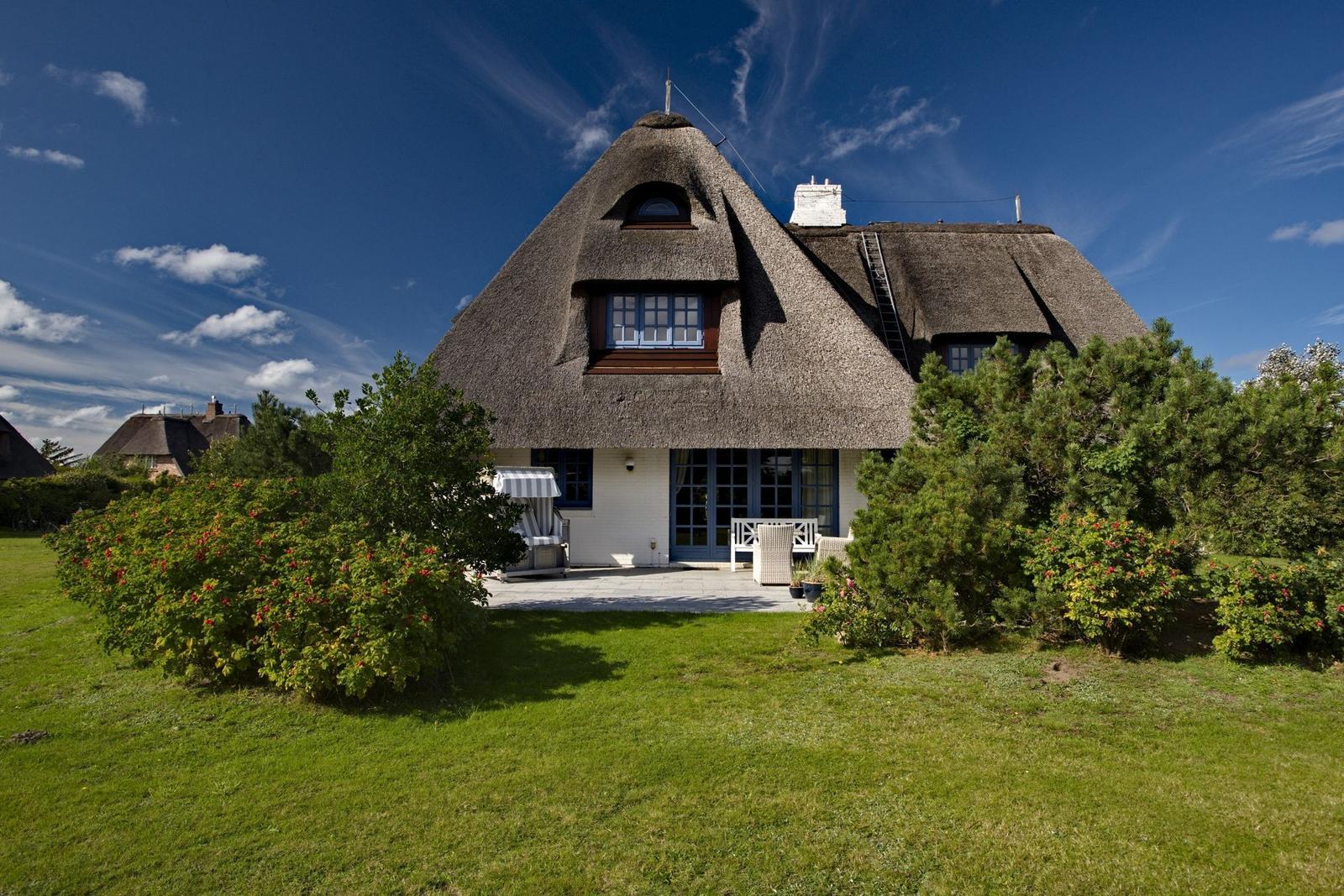 House with thatched roof, terrace, and garden under blue sky.