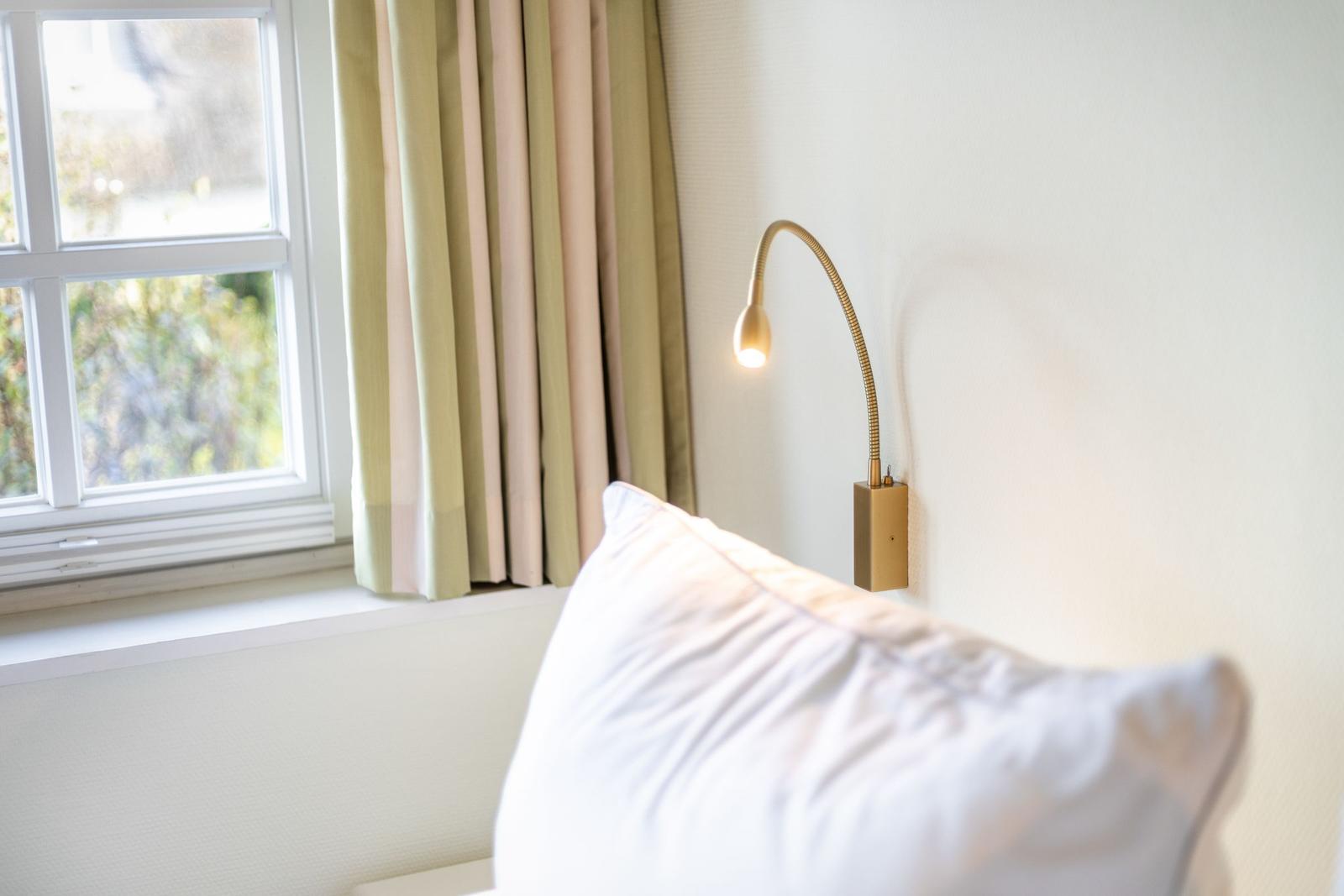 Ein Bett mit Kissen, Wandlampe und Fenster mit Vorhängen.