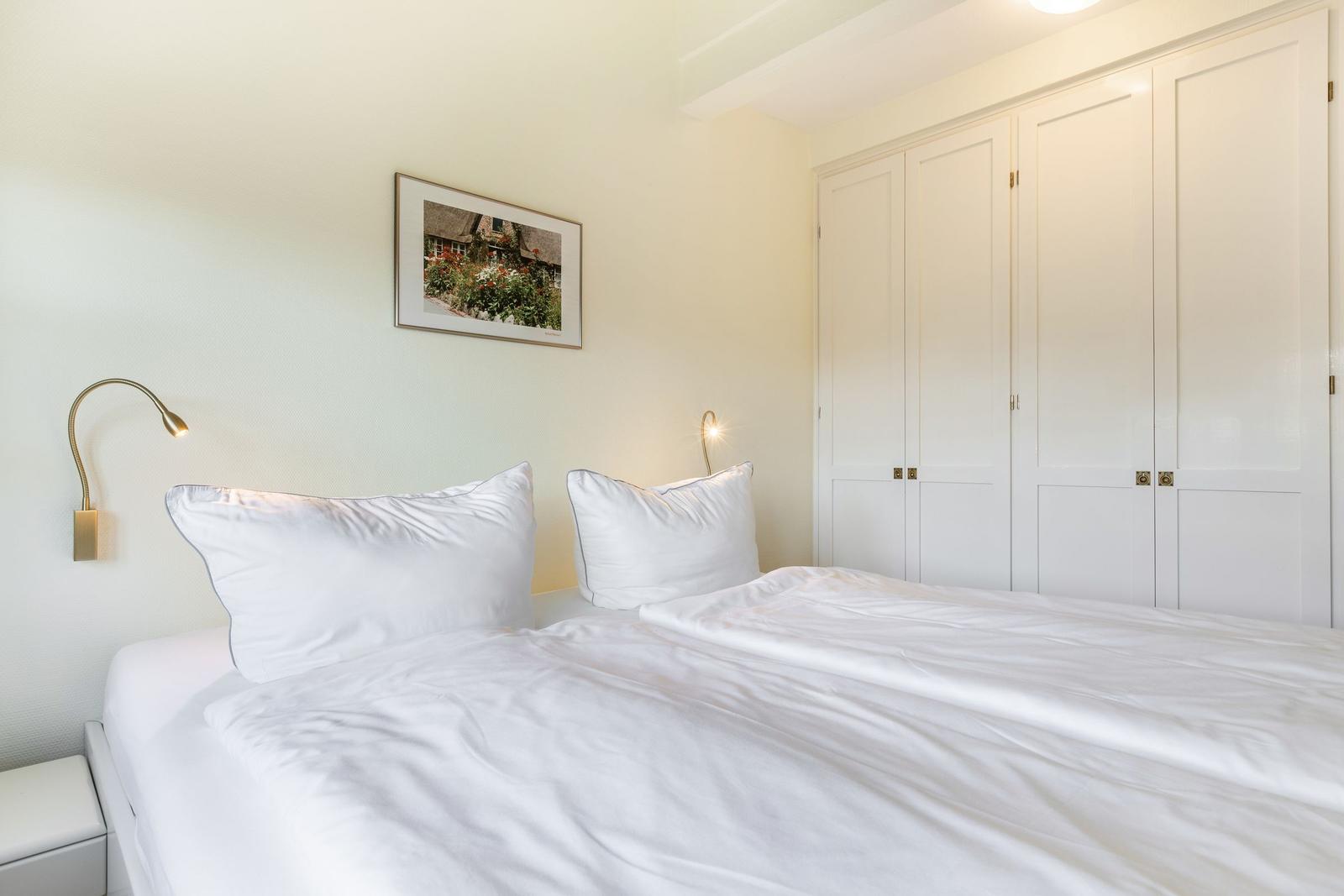 Schlafzimmer mit weißem Bett, Kleiderschrank und Wandbild.