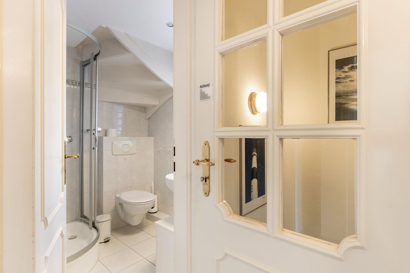 Badezimmer mit Dusche, Toilette und Waschbecken. Tür mit Glasfenstern.