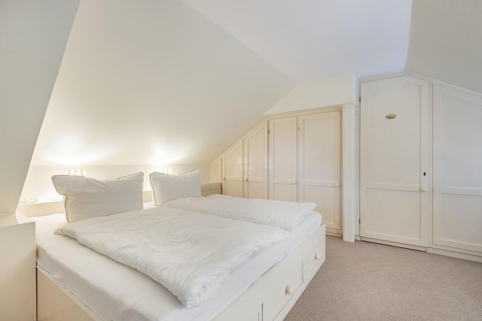 Schlafzimmer mit Doppelbett, weißen Schränken und schrägen Decken.