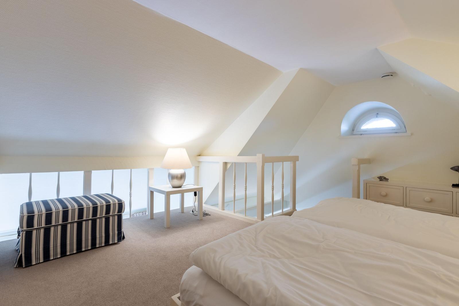 Schlafzimmer mit Dachschräge, Bett, Nachttisch, Lampe und Fenster.