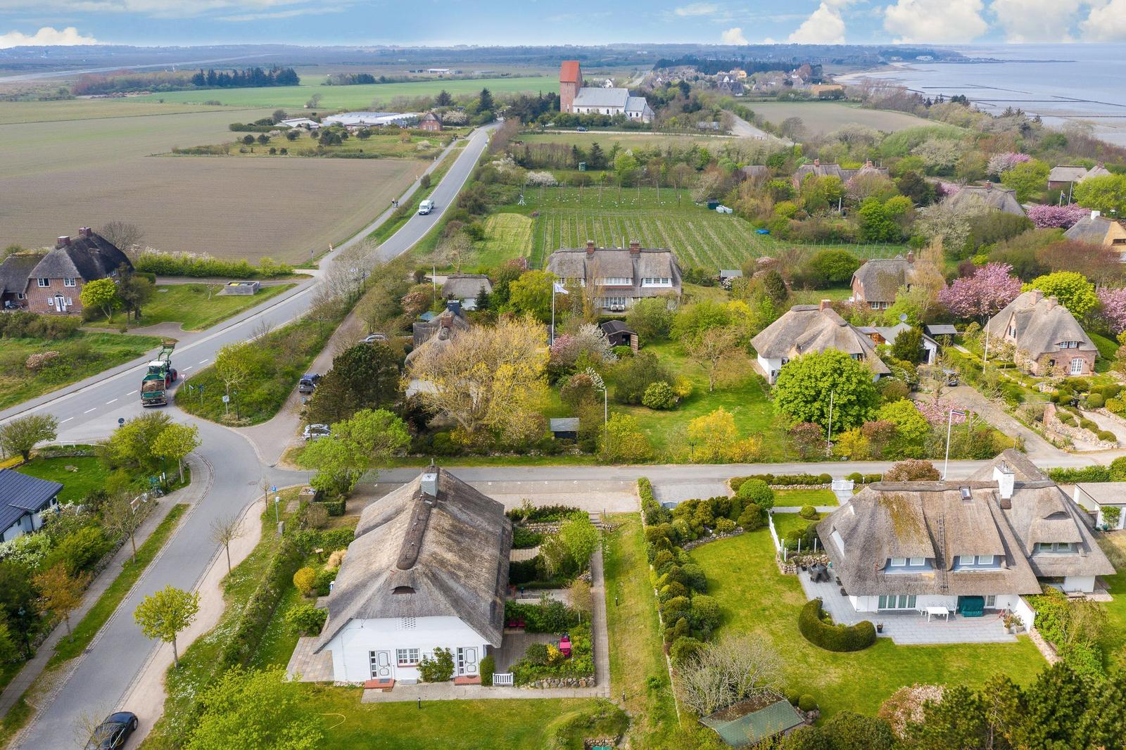 Dorf mit strohgedeckten Häusern und grünen Gärten. Straße führt zum Hafen.