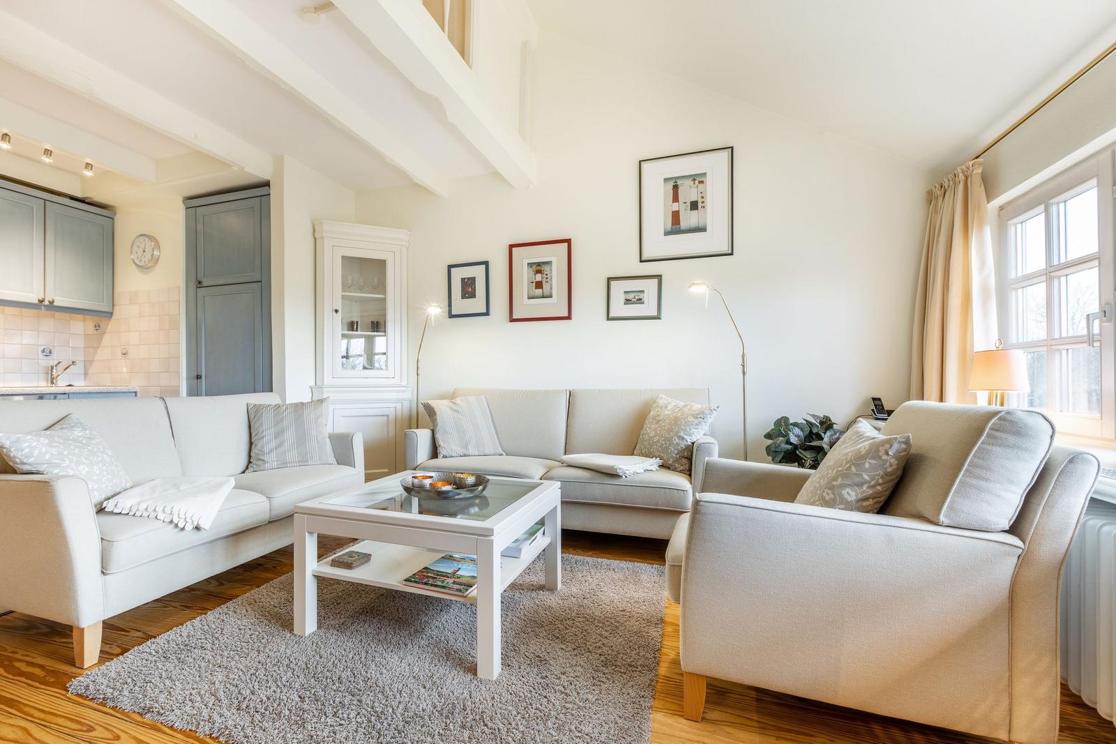 Wohnzimmer mit hellen Sofas, Glas-Tisch und Wandbildern.