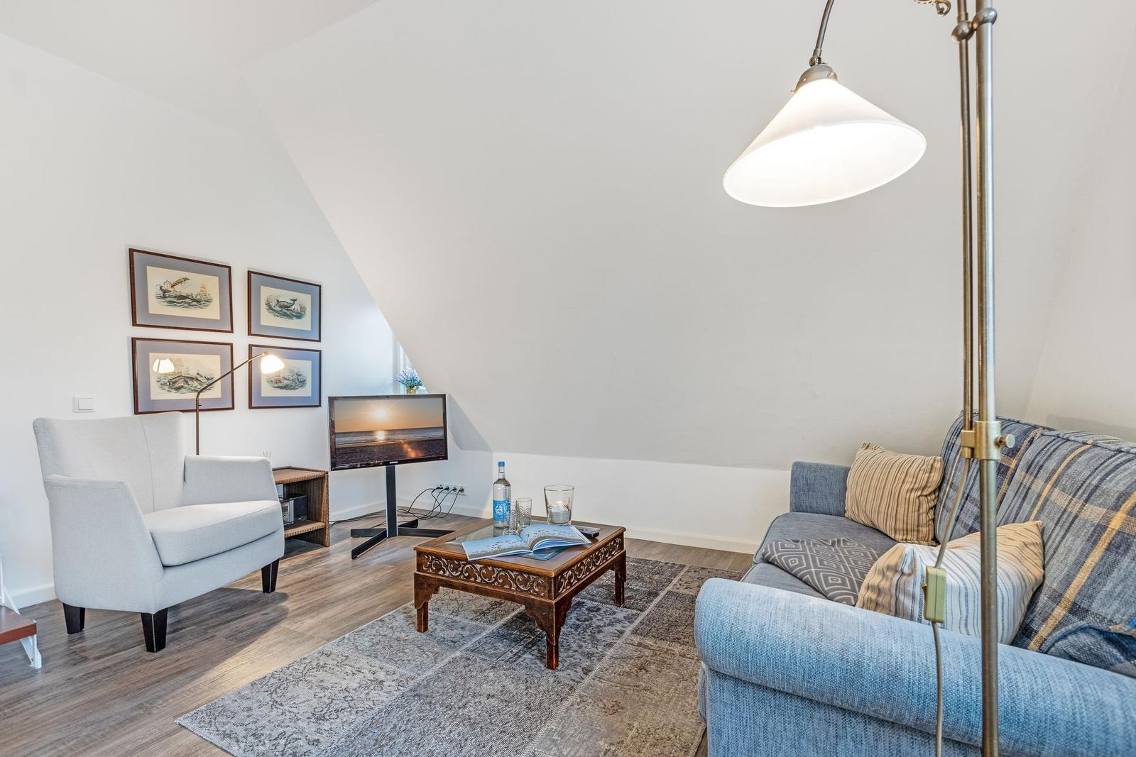 Living room with sofa, armchair, coffee table, and TV under sloped ceiling.