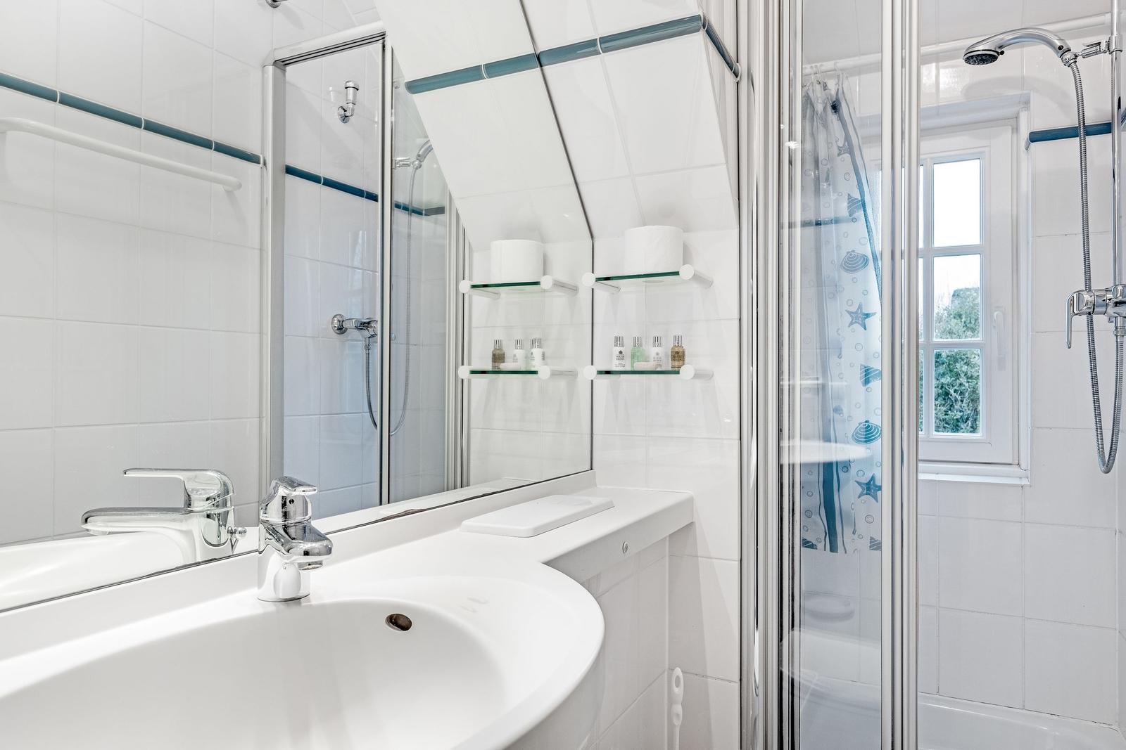 Bathroom with shower, sink, and mirror. Window with view of greenery.