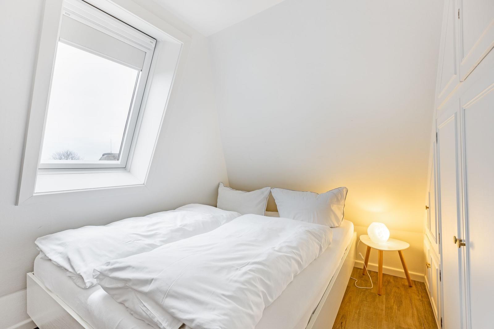 Bedroom with white bed, window, and nightstand with lamp.